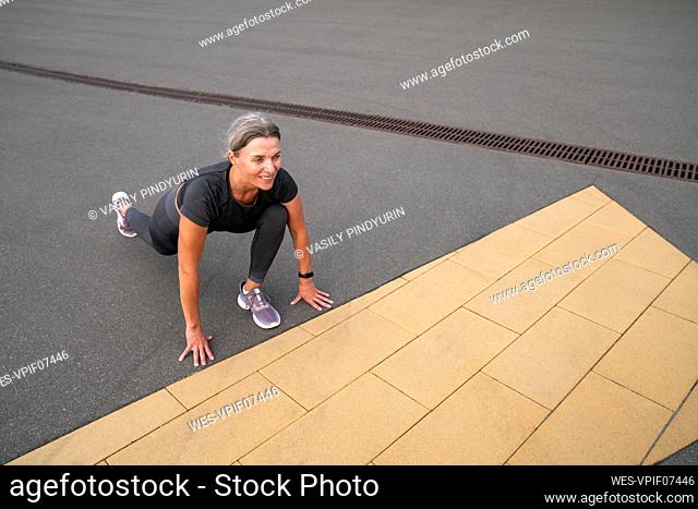 Smiling mature woman stretching on footpath