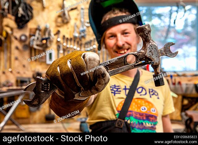 A front portrait view of a skilled tradesman showing his handmade multi-tool, consisting of a hammer, spanner and ratchet wrench welded together