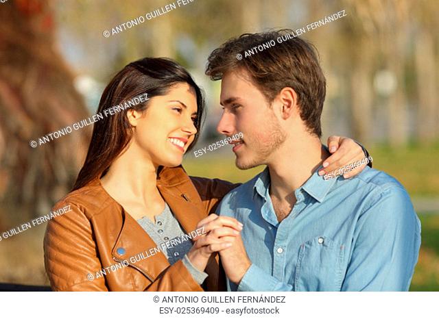 Couple in love hugging and dating sitting on a bench in a park looking each other
