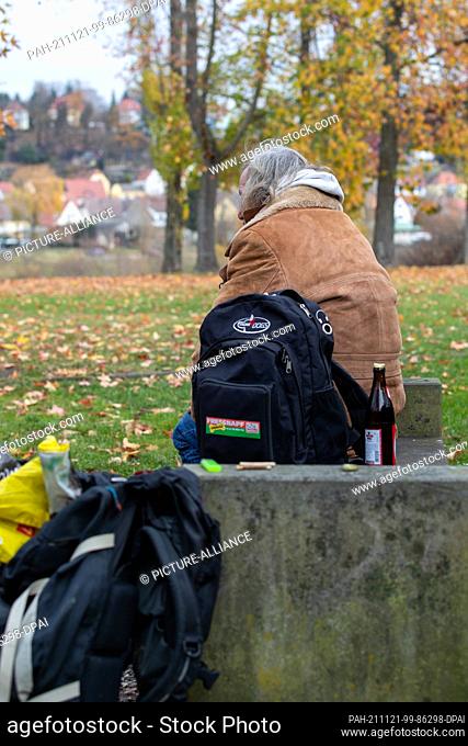 18 November 2021, Saxony, Pirna: An elderly man who has been homeless for many years sits on a park bench with his belongings