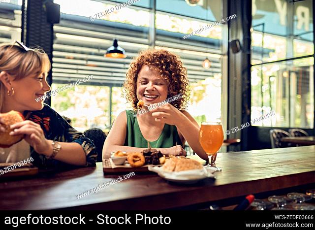 Two happy female friends having a snack at the counter in a pub