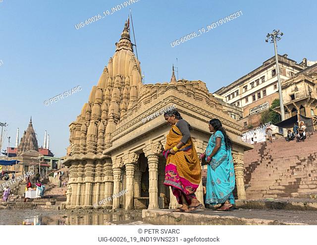 Two women in traditional sari dress in front of the leaning Ratneshwar Mahadev Temple, Varanasi, India