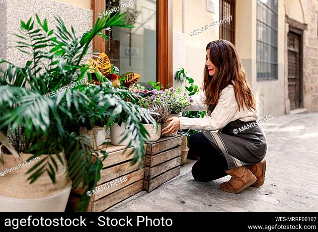 Female florist placing plants outside flower shop while crouching on street