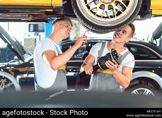 Two skilled auto mechanics analyzing together the rims of a lifted car while working in a modern automobile repair shop