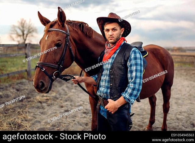 Cowboy in jeans and leather jacket poses with horse on texas farm, western. Vintage male person with animal, american culture