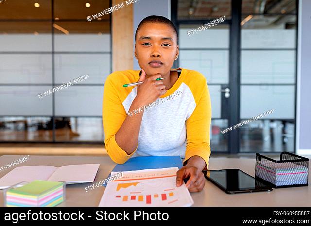 Portrait of confident african american businesswoman in casual sitting with chart in creative office