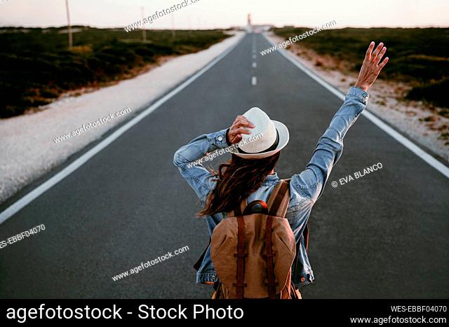 Backpacker with hand raised standing on road