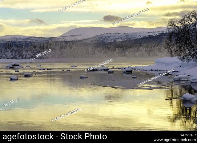 Winter landscape with river, sky reflecting in the water, nice warm colors, mountain in background, Tjåmmotis, Swedish Lapland, Sweden