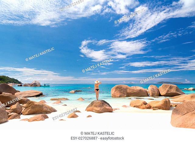 Woman wearing black bikini and beach hat, enjoying amazing view on Anse Lazio beach on Praslin Island, Seychelles. Summer vacations on picture perfect tropical...