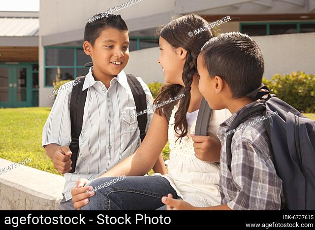 Cute brothers and sister talking, wearing backpacks ready for school