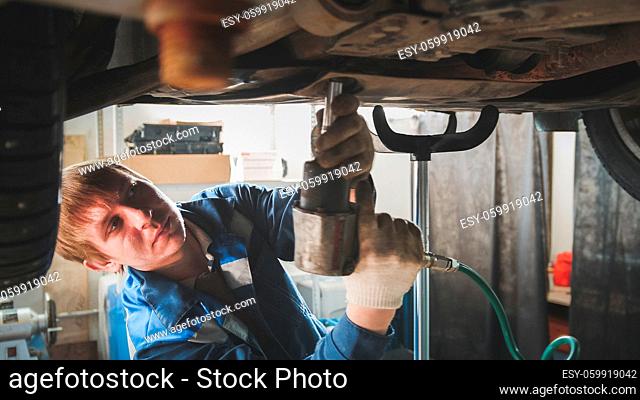 Mechanic with screwdriver in automobile garage - Man caucasian worker - repairing workshop - under lifted car, close up