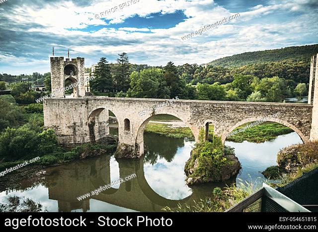 Besalu, Girona, Catalonia, Spain. Famous Landmark Old Medieval Romanesque Besalu Bridge Over The Fluvia River In Cloudy Summer Day