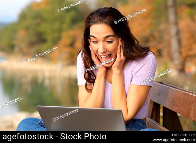 Surprised woman checking laptop in a lake on vacation