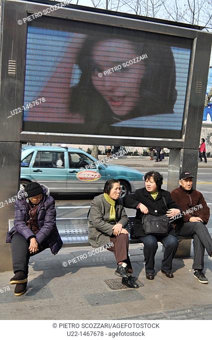 Shanghai (China): people sitting by an electronic ad along Middle Huai Hai Road