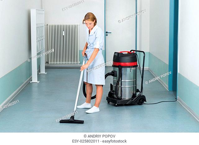 Young Female Cleaner In Uniform Vacuuming Floor