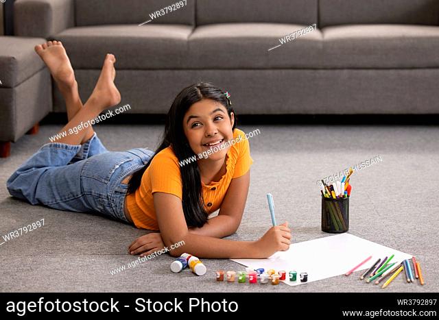 Portrait of a girl drawing on paper while lying down on floor in living room