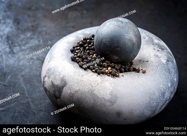 Modern design minimalistic mortar with black pepper berries as closeup on a rustic board with copy space left