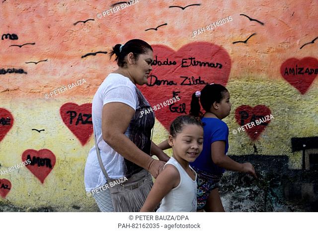 A family walks past a wall painted by peace activist Marieluce in the favela Complexo do Alemão in Rio de Janeiro, Brazil, 16 July 2016