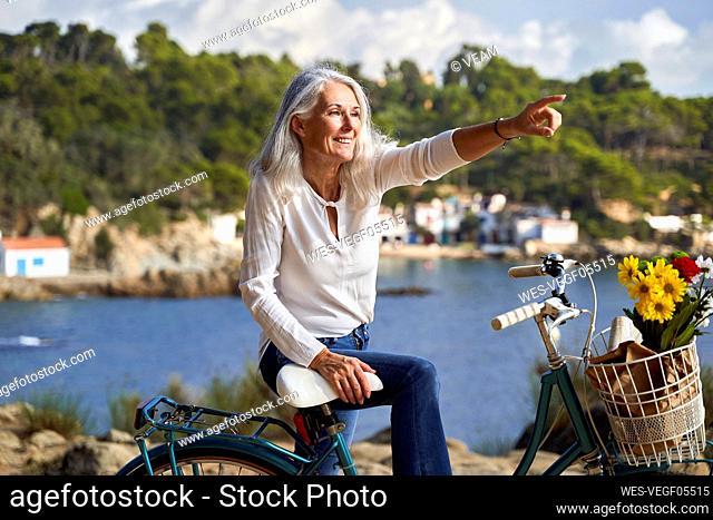 Happy woman standing with bicycle pointing away