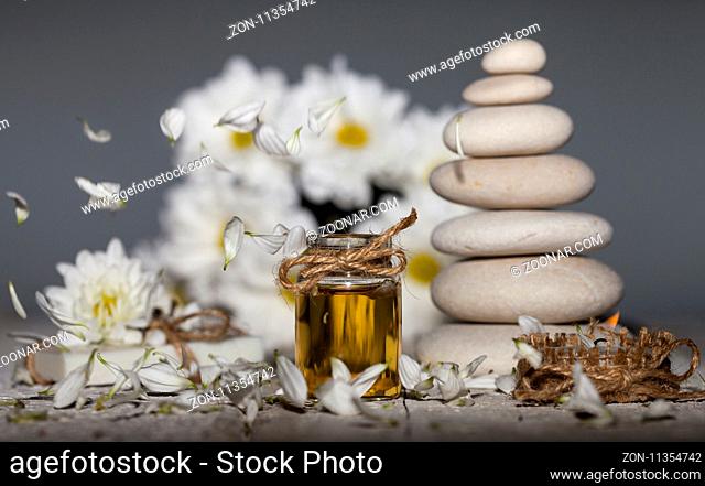 Spa background. Chamomile essential oil with fallen leaves, chamomile flowers and stack of white rocks on gray background