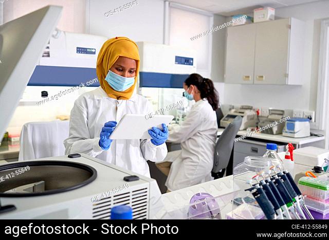 Female scientist in face mask and hijab using digital tablet in laboratory