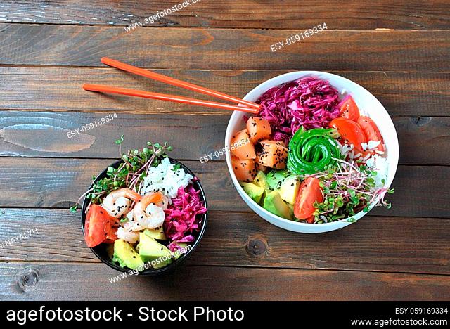 Organic food. Fresh seafood recipe. Two fresh poke bowls with salmon, shrimps, rice, red cabbage, avocado, cherry tomatoes and radish sprouts on wooden...