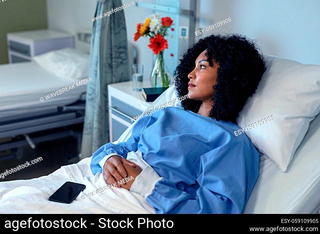 Thoughtful african american female patient lying in hospital bed with smartphone