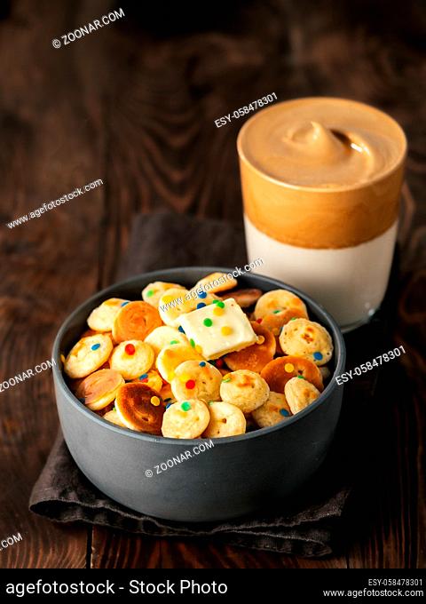 Mini pancakes cereal and dalgona coffee on brown wooden background, copy space. Trendy food and drink - tiny panckakes served sprinkles and whipped instant...