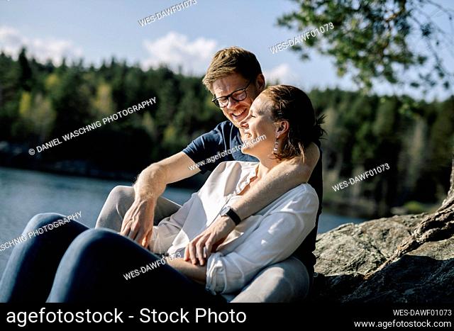 Happy couple sitting on a rock at the lakeside, Forstsee, Carinthia, Austria