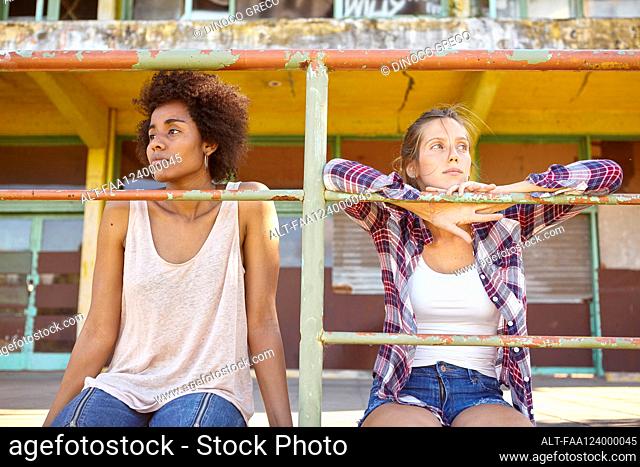 Young female friends sitting near railings outdoors