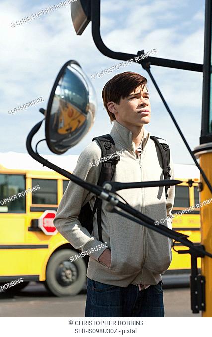 Male high school student standing outside school bus
