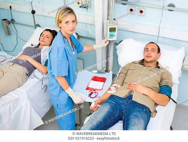 Nurse touching monitor next to transfused patients in hospital ward