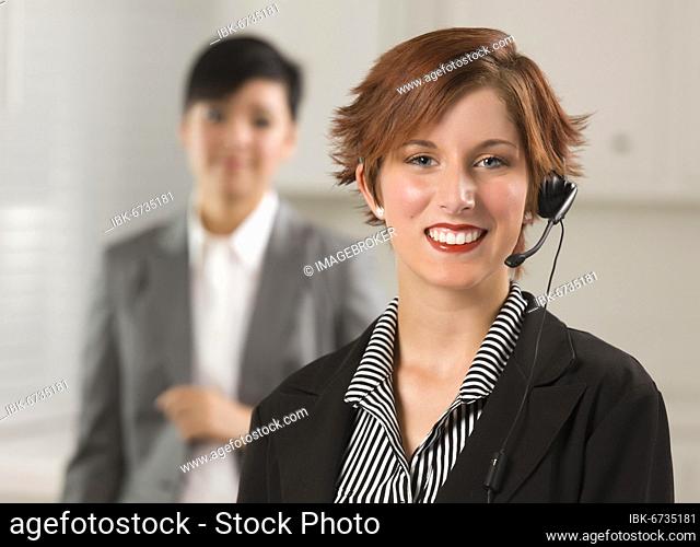 Pretty red haired businesswoman and colleague with headset in office setting