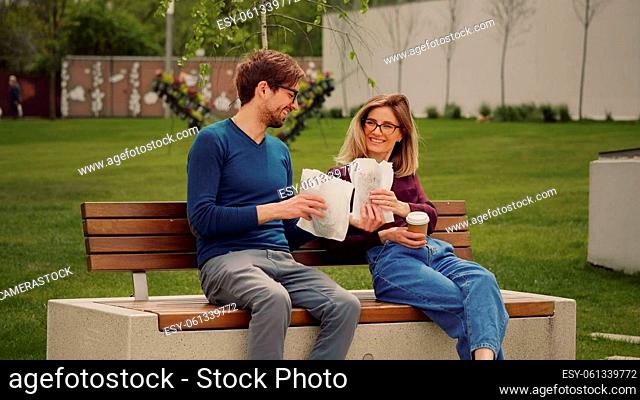 Handsome man brings lunch for colleague sitting on a bench in the park. Work Coffee Break. Student relaxing time. Outdoor walk. Take care concept