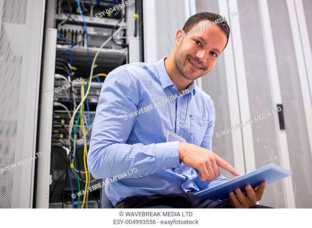Happy technician working on tablet pc beside servers in data center