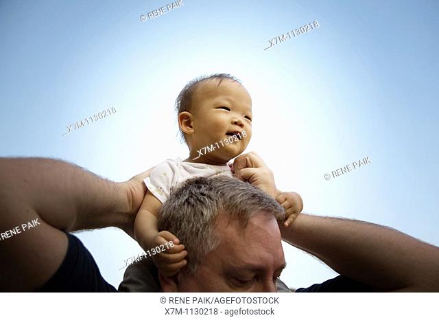 A Korean baby boy is given a ride on the shoulders of a large Caucasian man