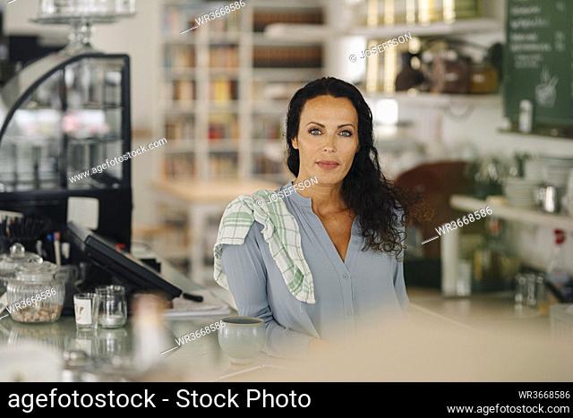 Confident female owner standing at counter in coffee shop