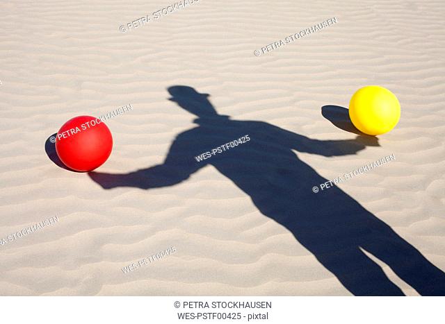 Shadow of man wearing a bowler hat and two balloons in sand