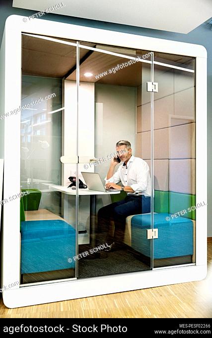 Businessman talking on mobile phone while sitting in cabin at office