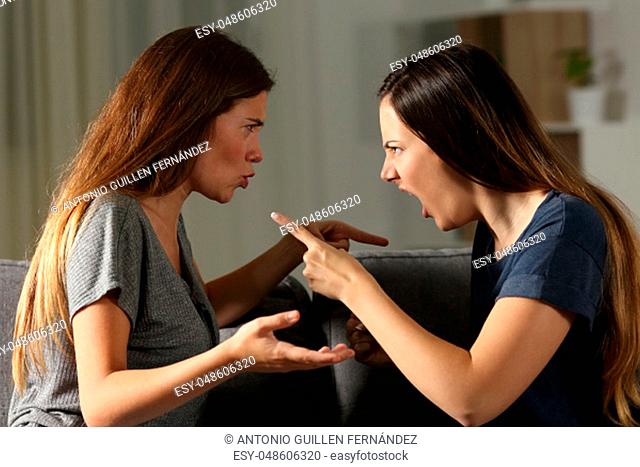 Side view portrait of two friends arguing and shouting in the night at home