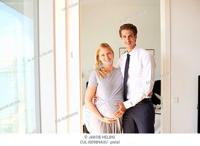 Portrait of pregnant couple with hands on her stomach in apartment