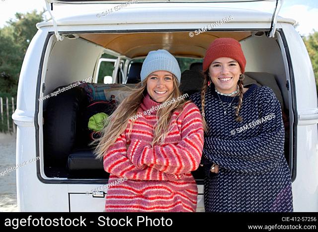 Portrait happy young women friends in knit hats at back of camper van