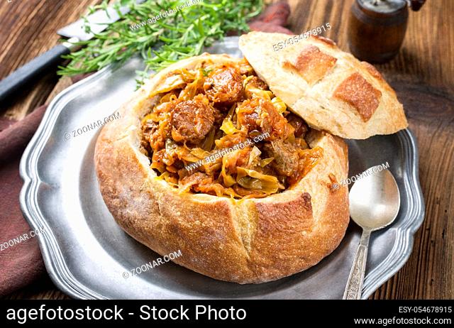 Traditional Polish kraut stew bigos with sausage and meat filled in white bread as closeup on a pewter plate