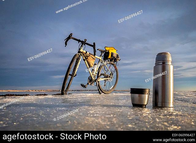 thermos bottle and cup of hot tea on an icy lake shore during winter biking, Boyd Lake State Park in northern Colorado