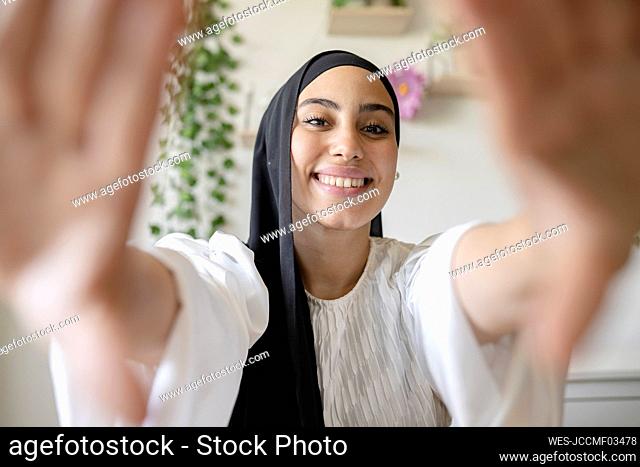 Smiling female freelancer making finger frame at home