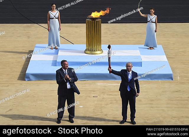 19 October 2021, Greece, Athen: Yu Zaiqing (R), vice president of the Chinese Olympic Committee, holds the torch during the ceremony to hand over the flame for...