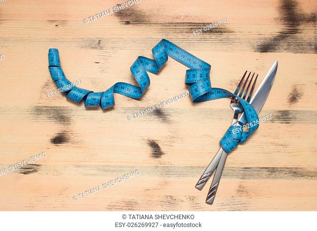 Knife and fork wrapped in blue tape measure on wooden table, diet concept