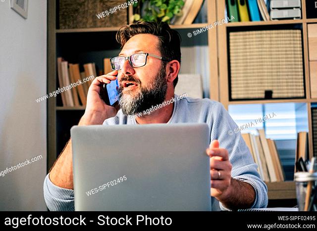 Male freelancer talking on smart phone while working at home
