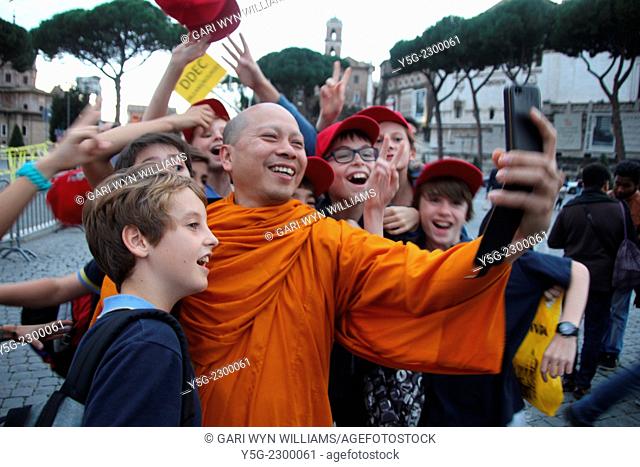 Rome, Italy 9th November 2014 - Buddhist monk taking a selfie photograph with group of children on Via dei Fori Imperiali street in Rome Italy