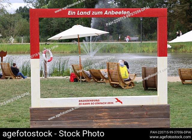 15 July 2022, Brandenburg, Beelitz: One frame reads ""A land to worship - Brandenburg it can be so simple"", while in the background there is a lake and a...